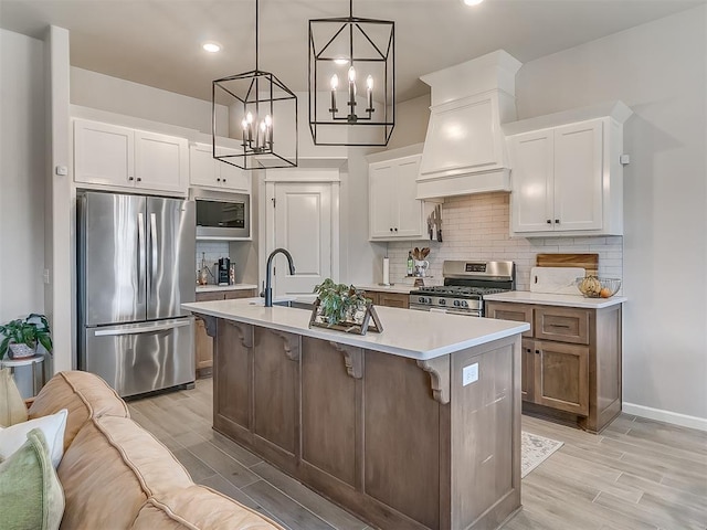 kitchen with decorative light fixtures, stainless steel appliances, light countertops, white cabinets, and an island with sink