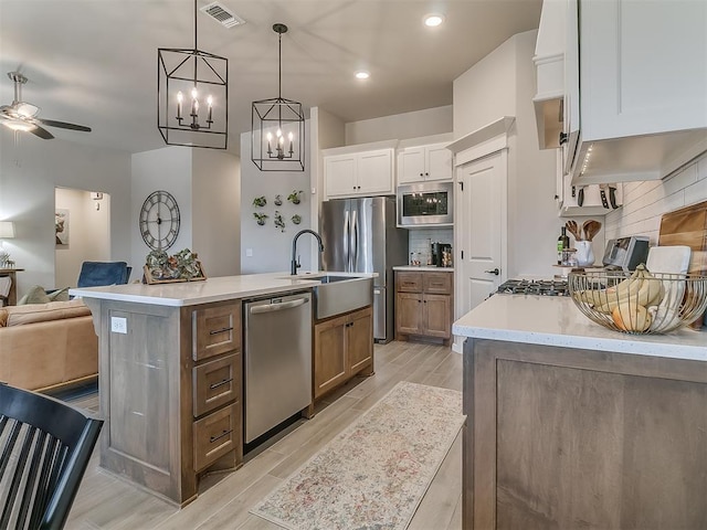 kitchen with brown cabinets, decorative light fixtures, appliances with stainless steel finishes, white cabinets, and an island with sink