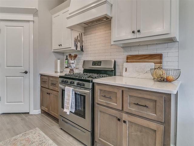 kitchen with decorative backsplash, white cabinets, brown cabinets, premium range hood, and stainless steel range with gas stovetop