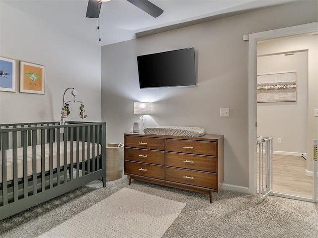 bedroom with light carpet, ceiling fan, a nursery area, and baseboards