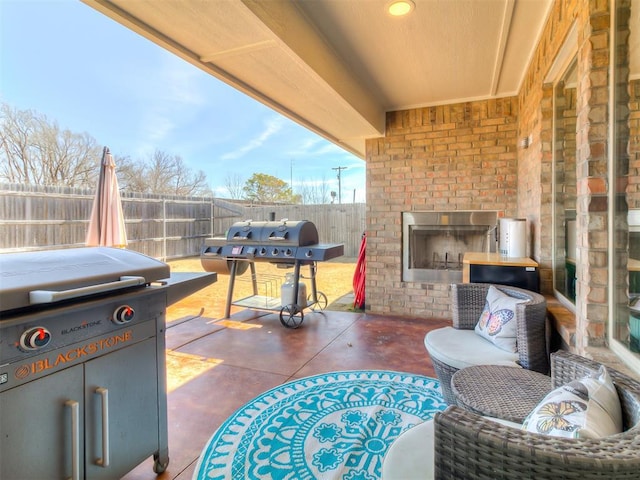 view of patio with an outdoor brick fireplace, a fenced backyard, and area for grilling