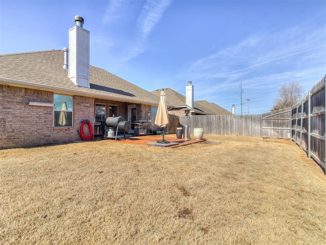 rear view of property featuring a fenced backyard, roof with shingles, a lawn, and brick siding