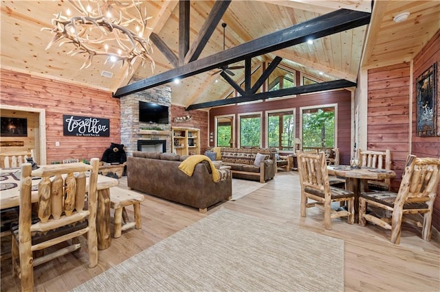 living room featuring a fireplace, wood walls, wood finished floors, high vaulted ceiling, and ceiling fan with notable chandelier