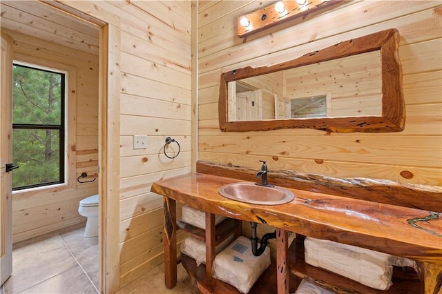 bathroom featuring toilet, wooden walls, and a sink