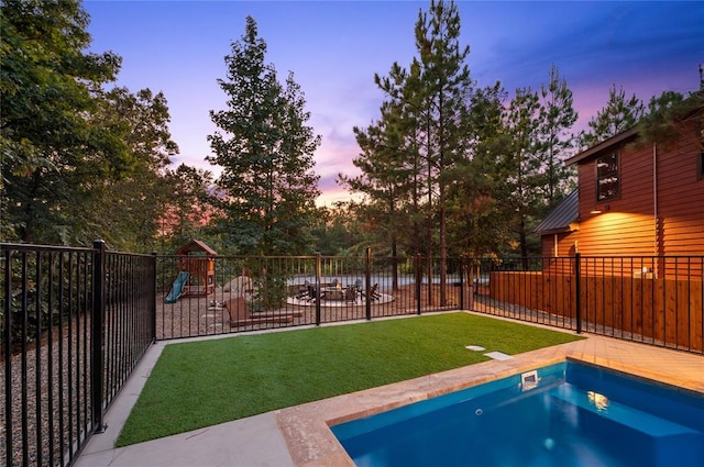 pool at dusk featuring a hot tub, fence, a playground, and a yard