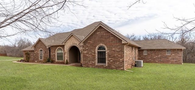 view of front of home featuring a front lawn, brick siding, central AC, and roof with shingles