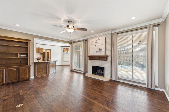 unfurnished living room featuring dark wood finished floors, a fireplace, crown molding, and a ceiling fan