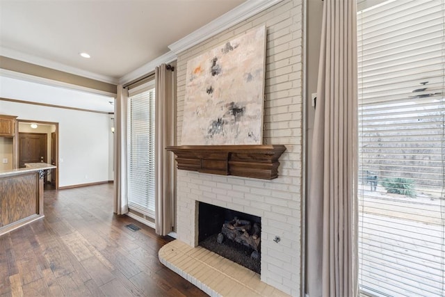 living area featuring visible vents, baseboards, dark wood-style flooring, ornamental molding, and a brick fireplace