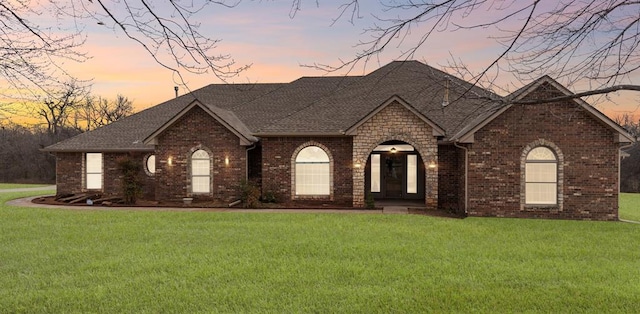 view of front facade with a yard, brick siding, and a shingled roof