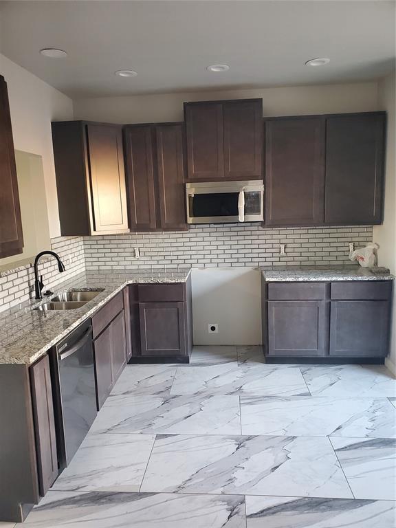 kitchen featuring light stone counters, marble finish floor, stainless steel appliances, dark brown cabinetry, and a sink