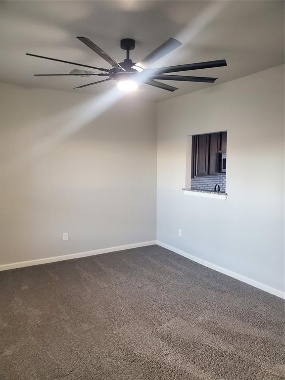 empty room featuring dark carpet, a ceiling fan, and baseboards