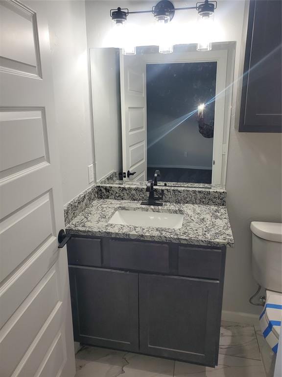 half bath featuring toilet, marble finish floor, baseboards, and vanity