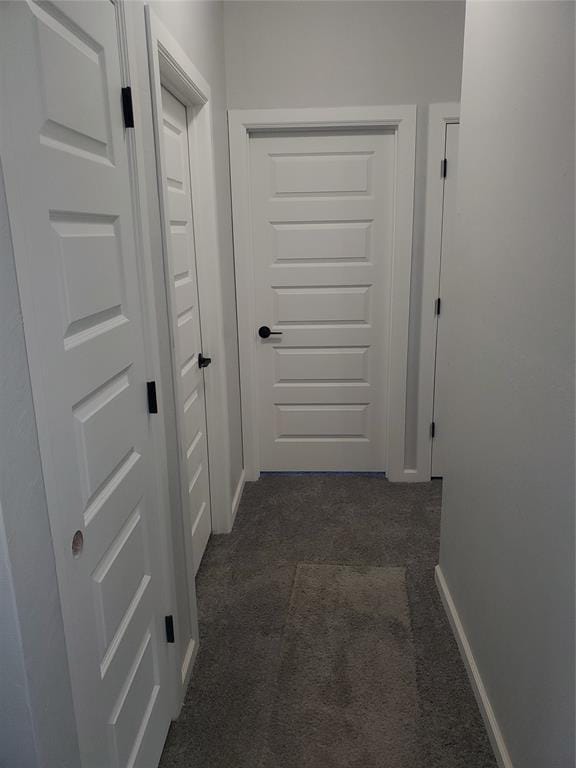 hallway featuring dark colored carpet and baseboards