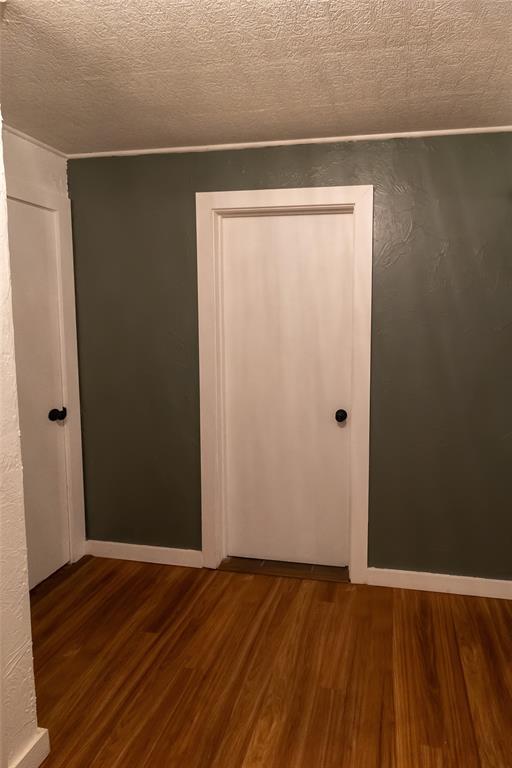 unfurnished bedroom featuring a textured ceiling, baseboards, and wood finished floors