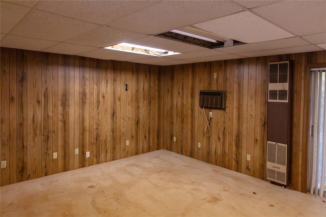 empty room with a paneled ceiling, a heating unit, and wooden walls