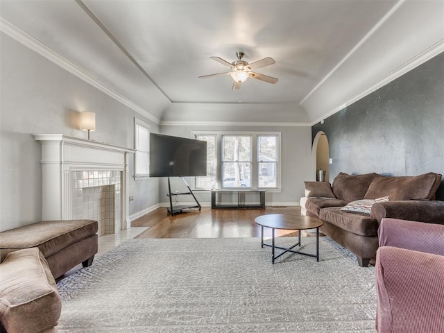 living area featuring arched walkways, ceiling fan, wood finished floors, and crown molding