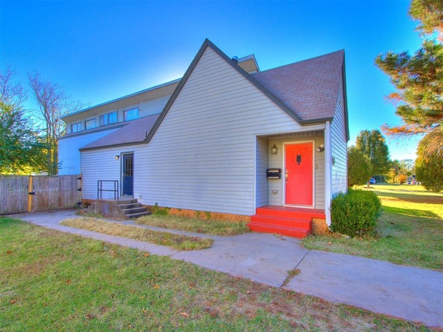 view of front facade with a shingled roof, a front yard, fence, and entry steps