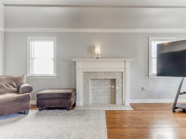 living room featuring ornamental molding, a tiled fireplace, baseboards, and wood finished floors