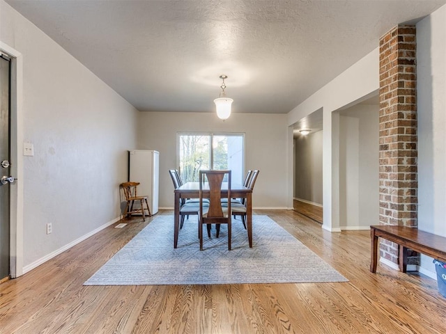 dining room with light wood finished floors, baseboards, and a textured ceiling