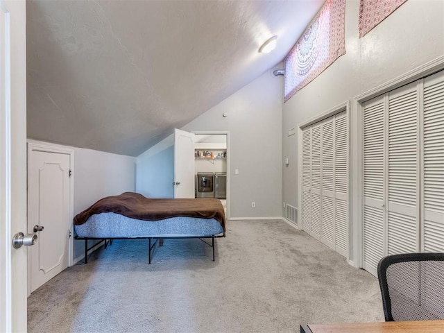 bedroom with light carpet, separate washer and dryer, visible vents, vaulted ceiling, and two closets