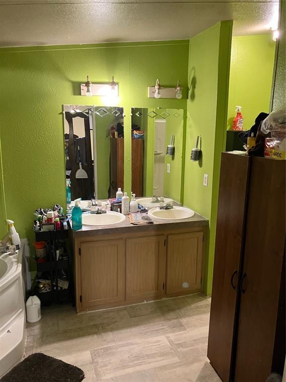 full bath featuring a textured wall, double vanity, a textured ceiling, and a sink