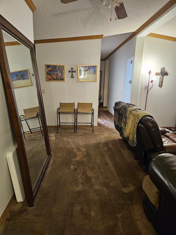 hall with dark colored carpet, crown molding, and a textured ceiling