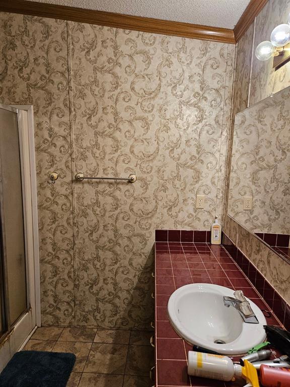 full bathroom featuring ornamental molding, tile patterned floors, a textured ceiling, a shower stall, and a sink