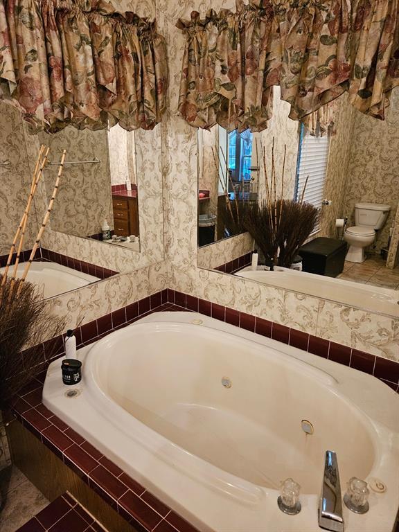 full bathroom featuring toilet, wallpapered walls, and a garden tub