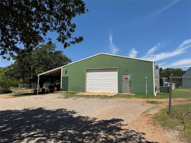 detached garage with dirt driveway, fence, and a carport