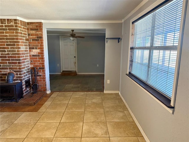 unfurnished living room featuring ornamental molding, a wood stove, light tile patterned flooring, ceiling fan, and baseboards