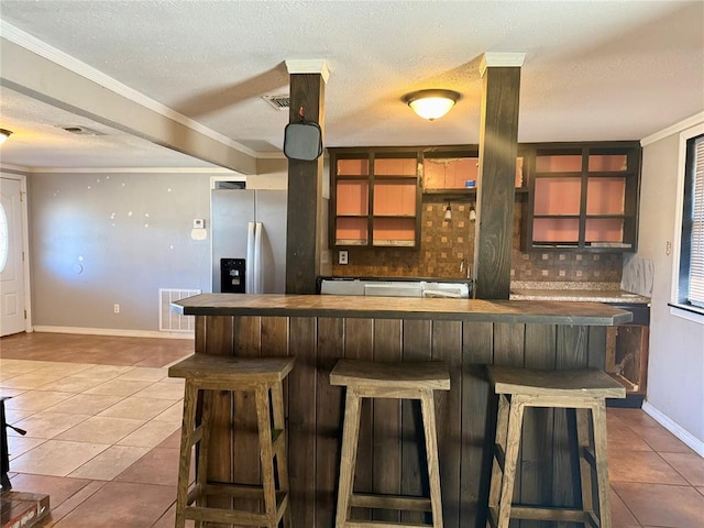 kitchen with tile patterned floors, stainless steel fridge, visible vents, and a kitchen breakfast bar