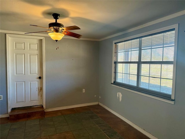 empty room with a ceiling fan, dark tile patterned flooring, crown molding, and baseboards