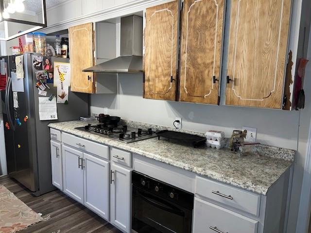 kitchen with light stone countertops, appliances with stainless steel finishes, dark wood-style floors, and wall chimney range hood