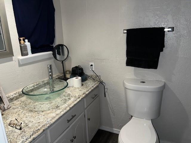 bathroom with baseboards, toilet, vanity, and a textured wall