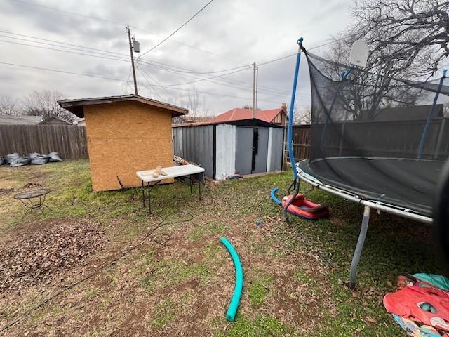 view of yard featuring an outdoor structure, a storage unit, a fenced backyard, and a trampoline