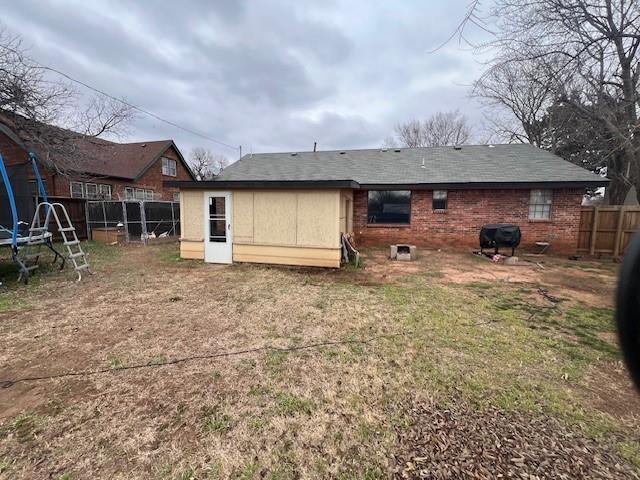 back of house featuring a trampoline, brick siding, and fence