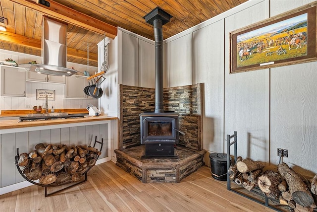 interior details featuring island range hood, wood ceiling, wood finished floors, a wood stove, and stainless steel gas stovetop