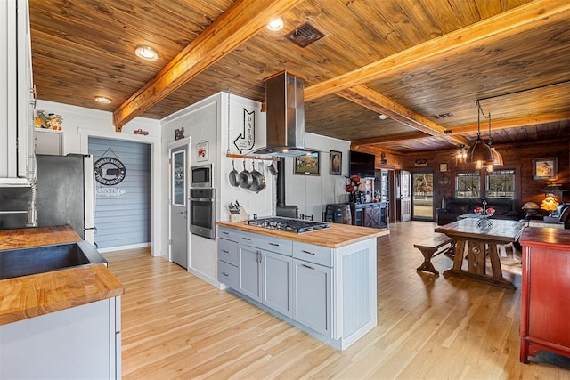 kitchen featuring island range hood, light wood-style floors, wooden counters, appliances with stainless steel finishes, and beamed ceiling