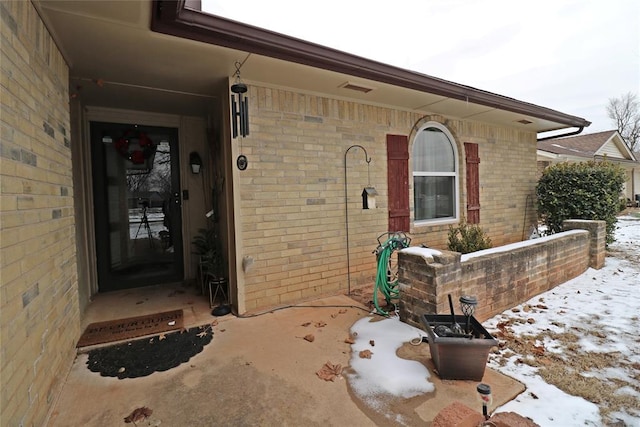 snow covered property entrance featuring brick siding