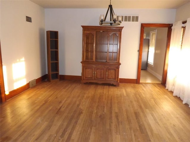 interior space featuring light wood finished floors, baseboards, visible vents, and an inviting chandelier