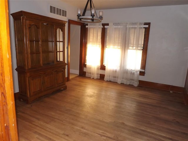 unfurnished dining area featuring a chandelier, visible vents, baseboards, and wood finished floors