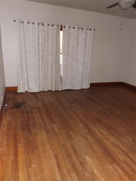 empty room featuring a ceiling fan, baseboards, and wood finished floors