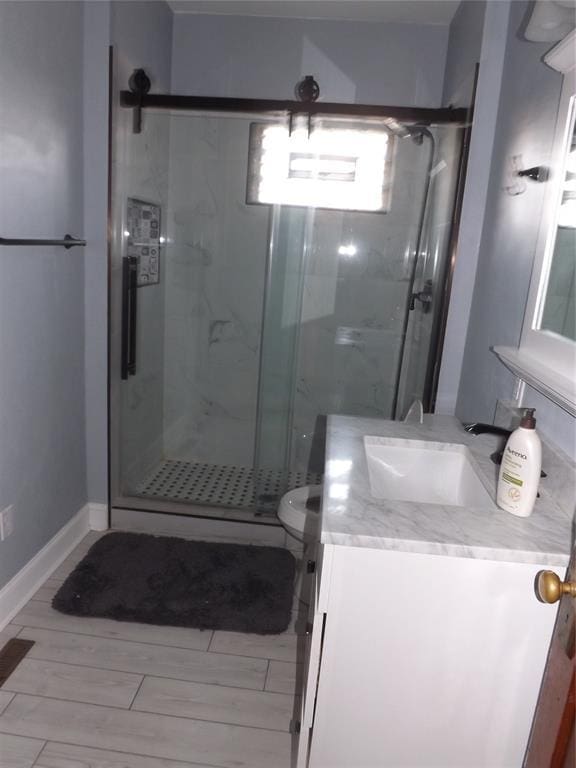 bathroom featuring toilet, wood tiled floor, a shower stall, vanity, and baseboards