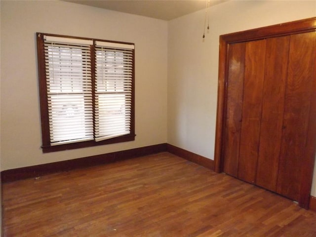 unfurnished bedroom with a closet, baseboards, and dark wood-style flooring