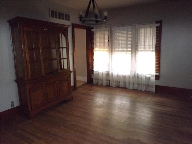 unfurnished dining area with a chandelier, visible vents, dark wood finished floors, and baseboards