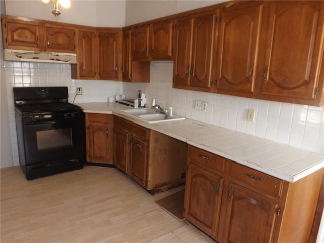 kitchen featuring ventilation hood, gas stove, a sink, and brown cabinets