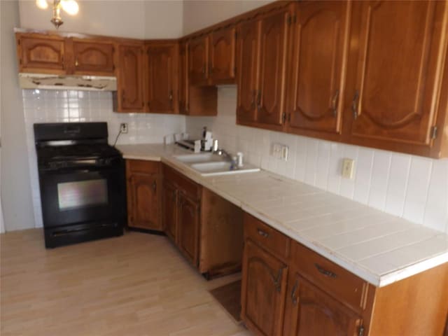 kitchen featuring brown cabinetry, a sink, and black range