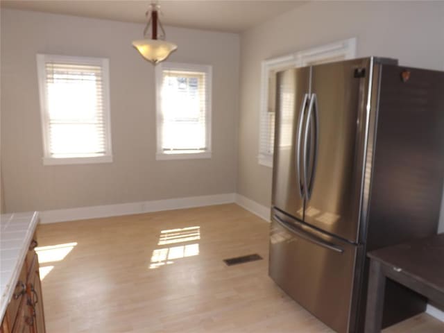 kitchen featuring visible vents, tile counters, freestanding refrigerator, hanging light fixtures, and a wealth of natural light