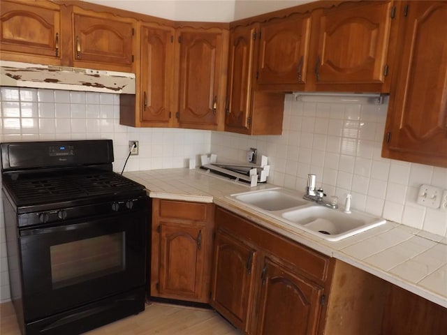 kitchen featuring tile counters, black range with gas stovetop, ventilation hood, and a sink