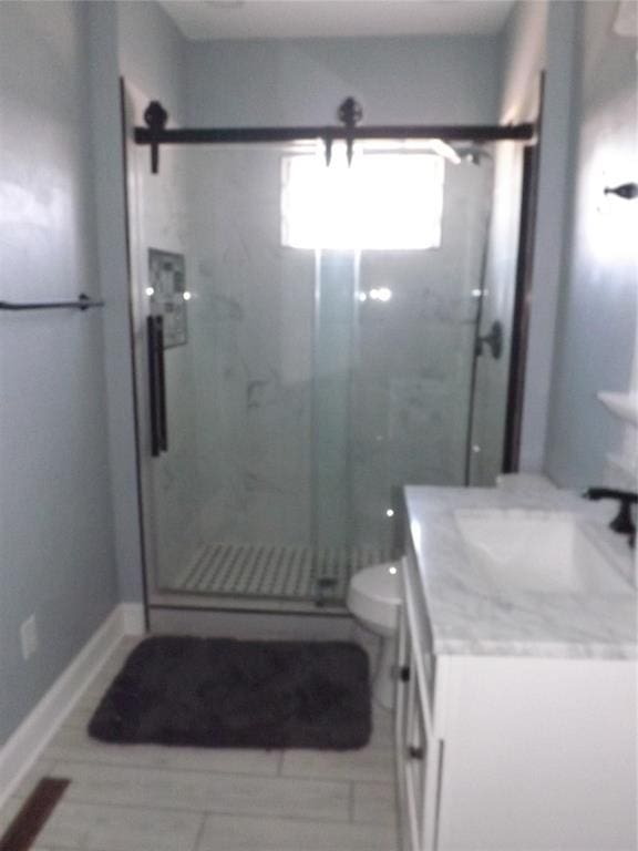 bathroom featuring a stall shower, vanity, toilet, and baseboards